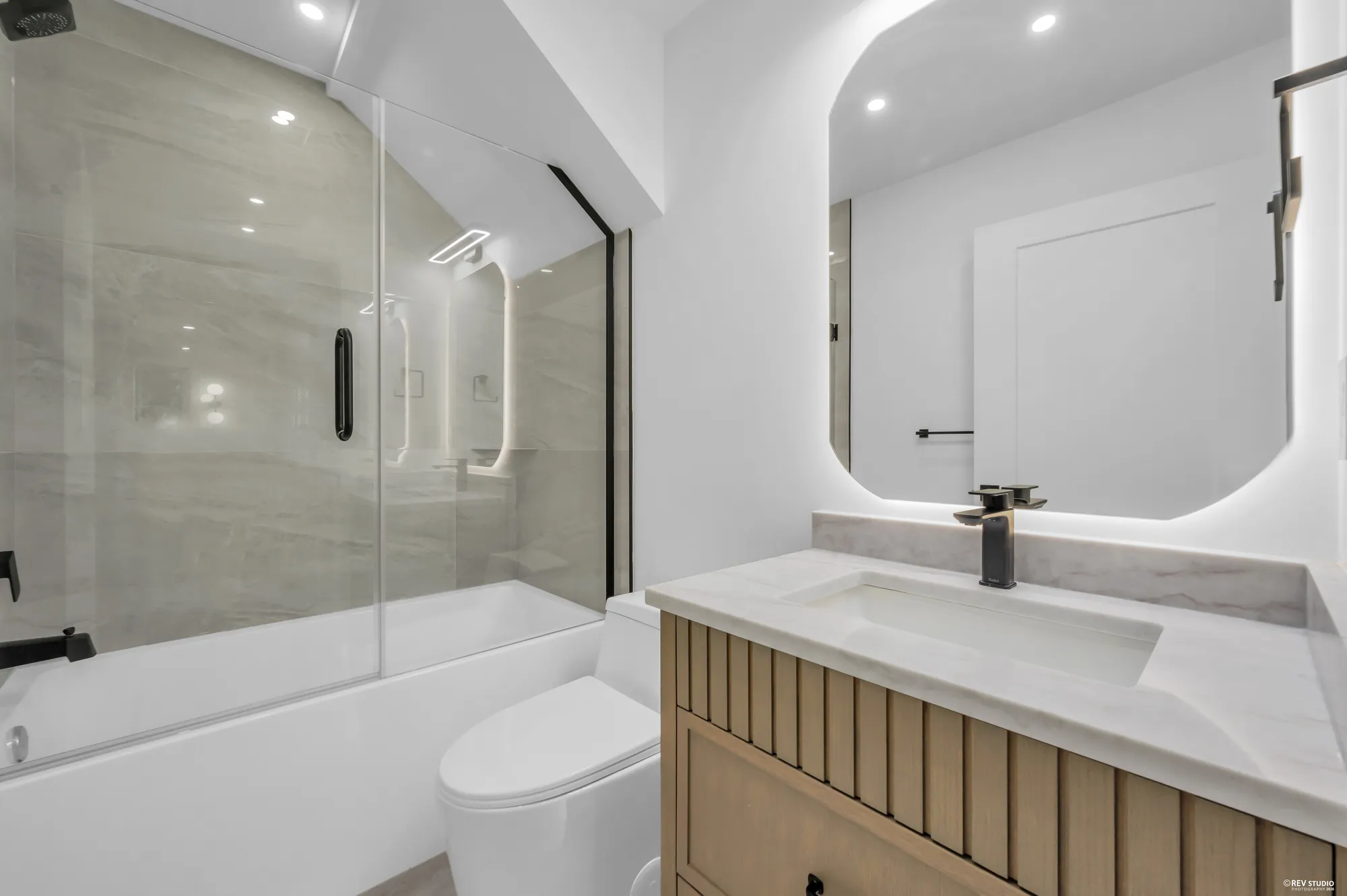 Bathroom with a tub under a glass screen and a stone-topped vanity