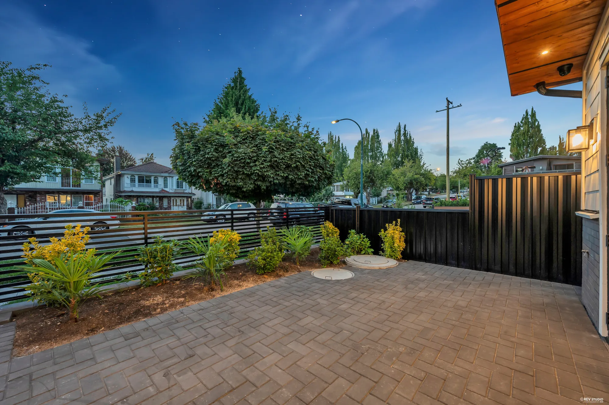 The paved patio with young planting along a timber fence