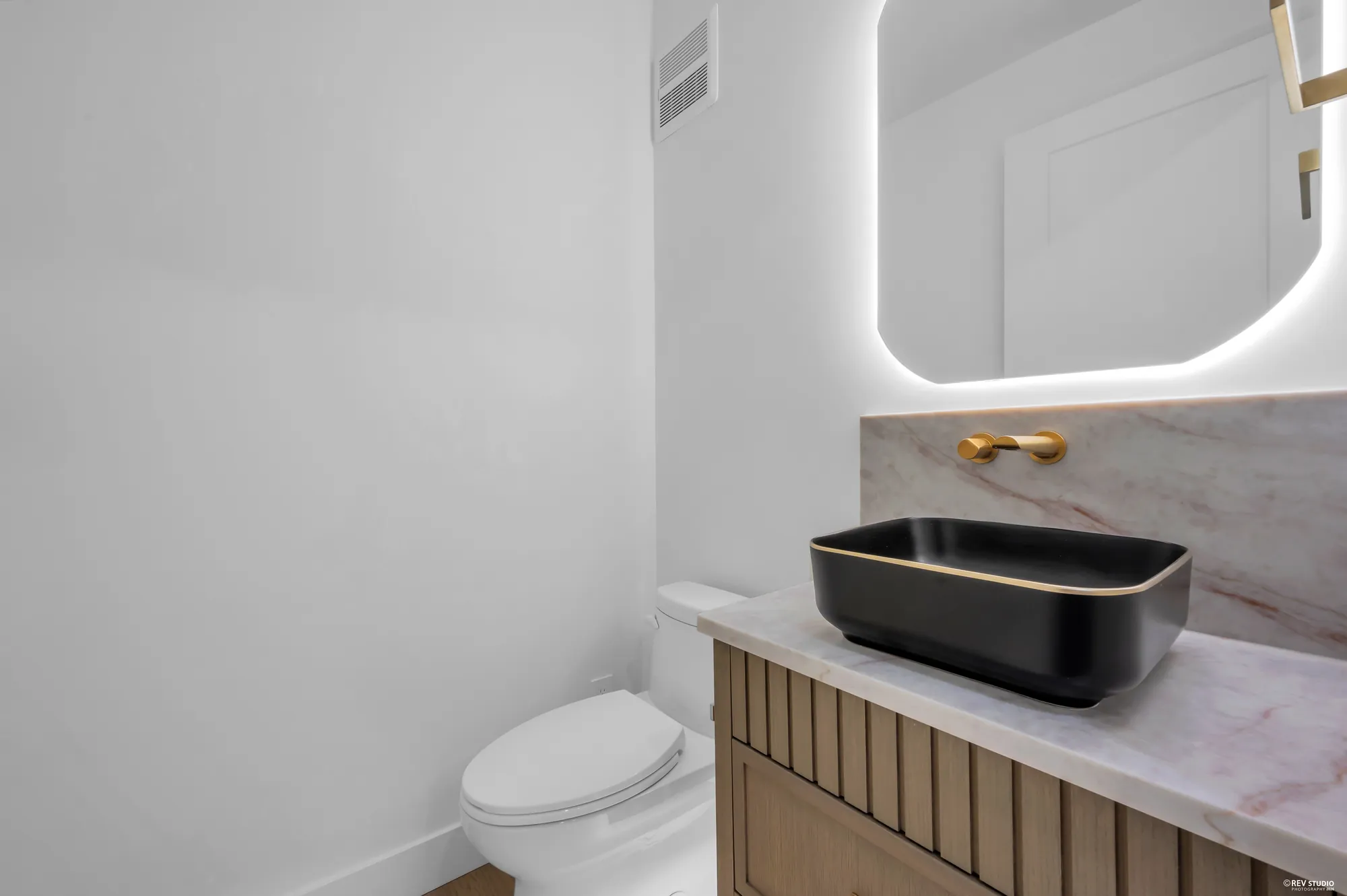 Powder room with a dark vessel basin and a backlit mirror